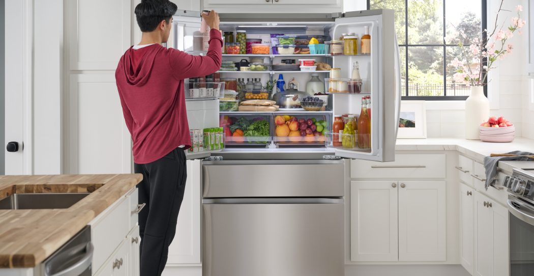 a man in a red hoodie putting food into a french door stainless steel refrigerator with a bottom freezer